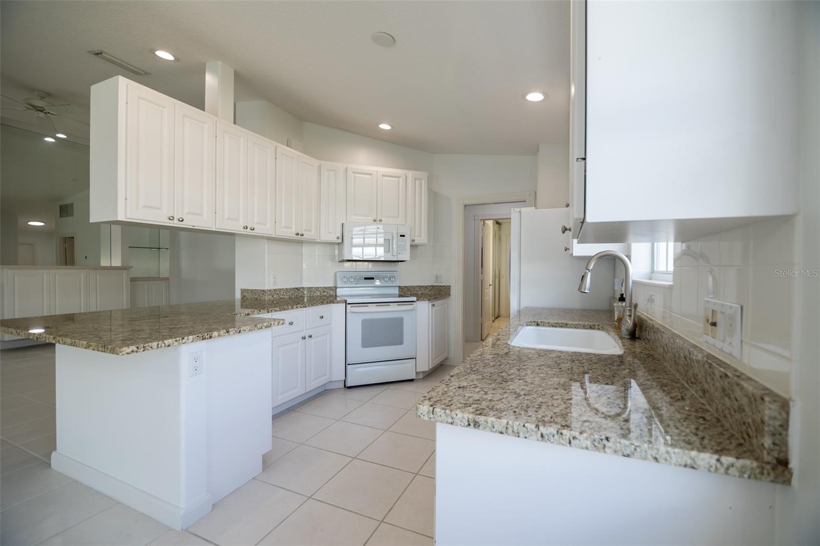 Bright kitchen with white cabinets, granite counters, breakfast bar, and electric range.
