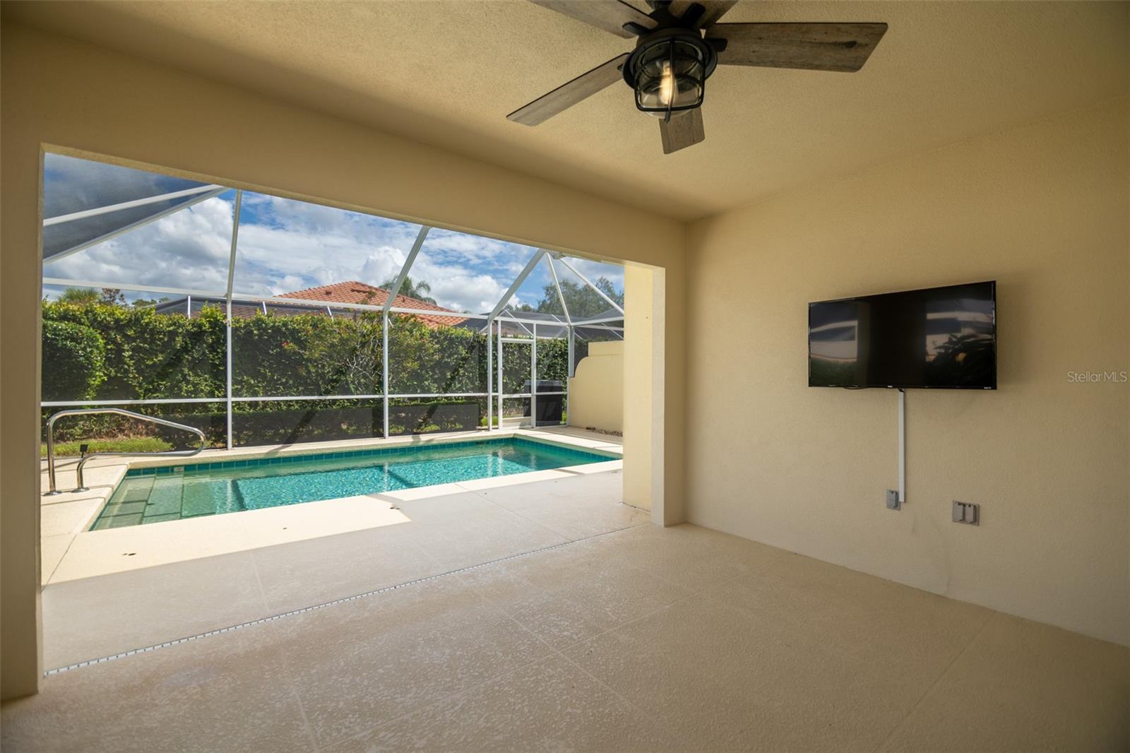 Covered lanai with a screened swimming pool, tiled deck, ceiling fan, and wall-mounted television.