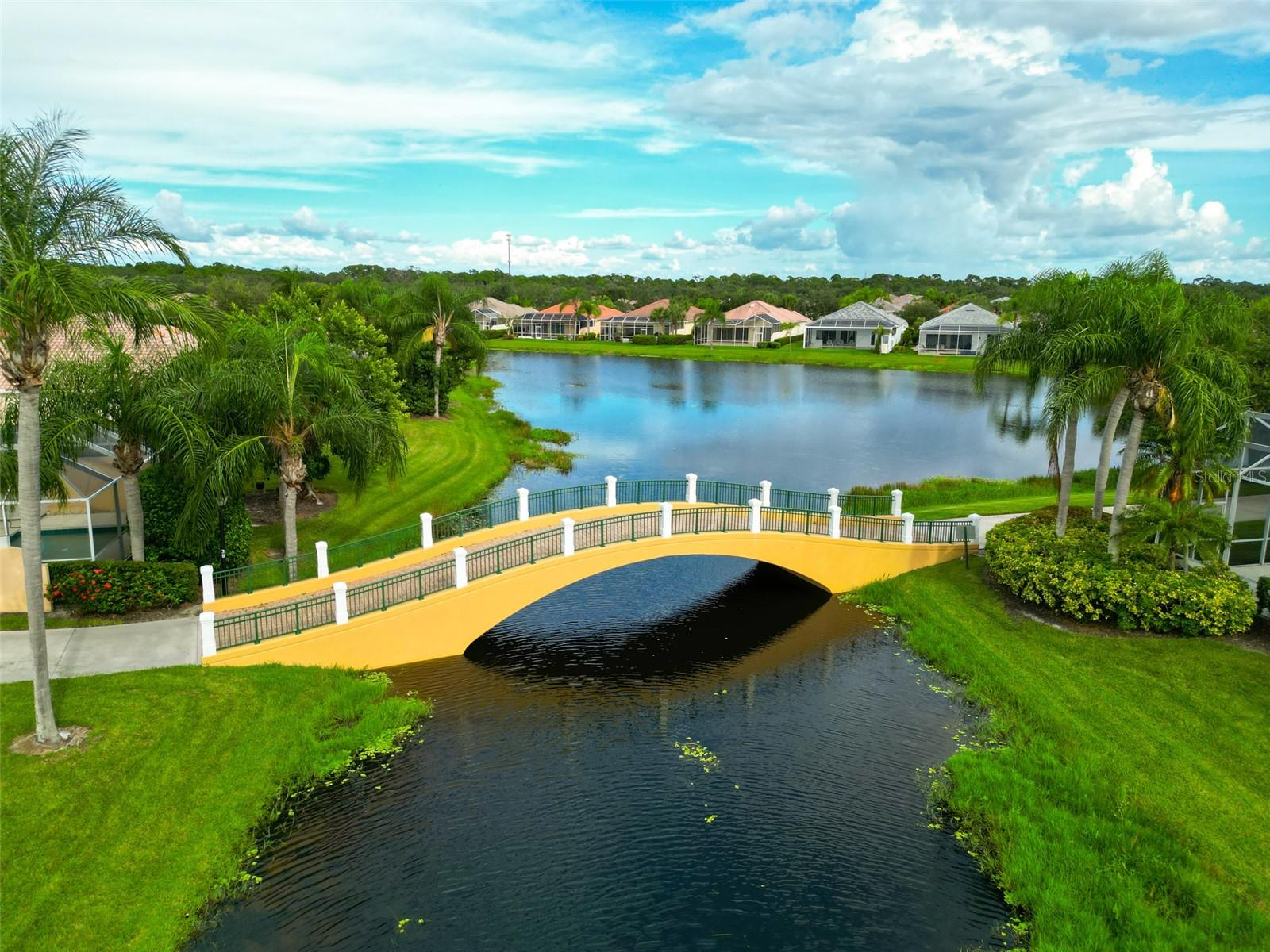 Aerial view of a residential canal and pond, with a yellow arched bridge and palm trees.