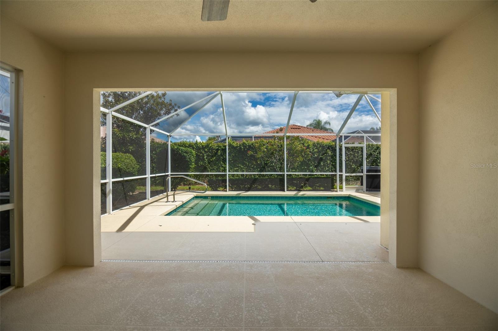 Screened swimming pool and tiled patio viewed from a covered lanai.
