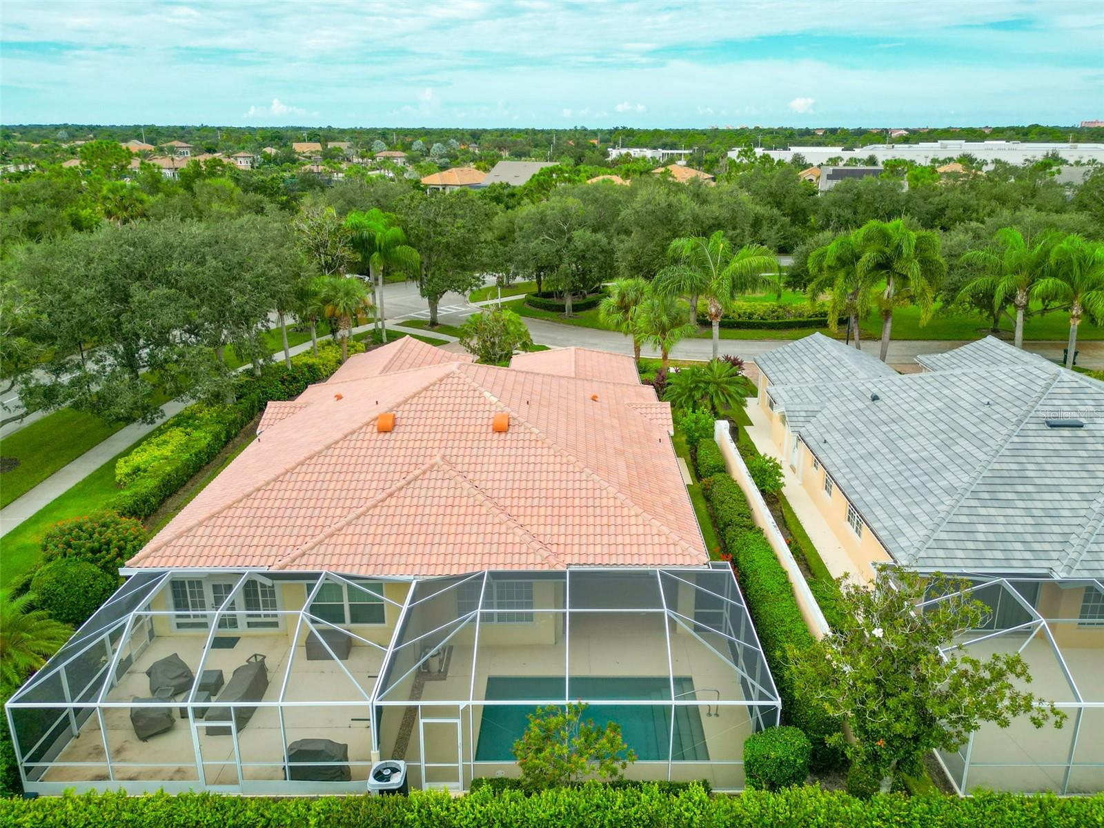 Aerial view of the home's screened pool enclosure, tiled roof, and surrounding palms.