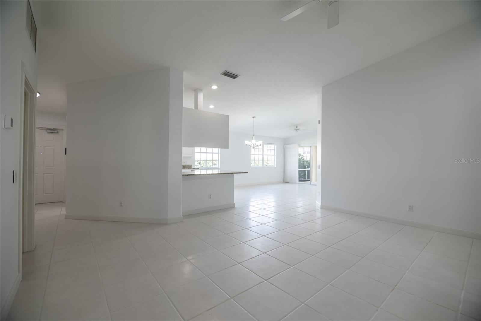 Empty open-plan living and dining area with large tile floors and a kitchen peninsula.