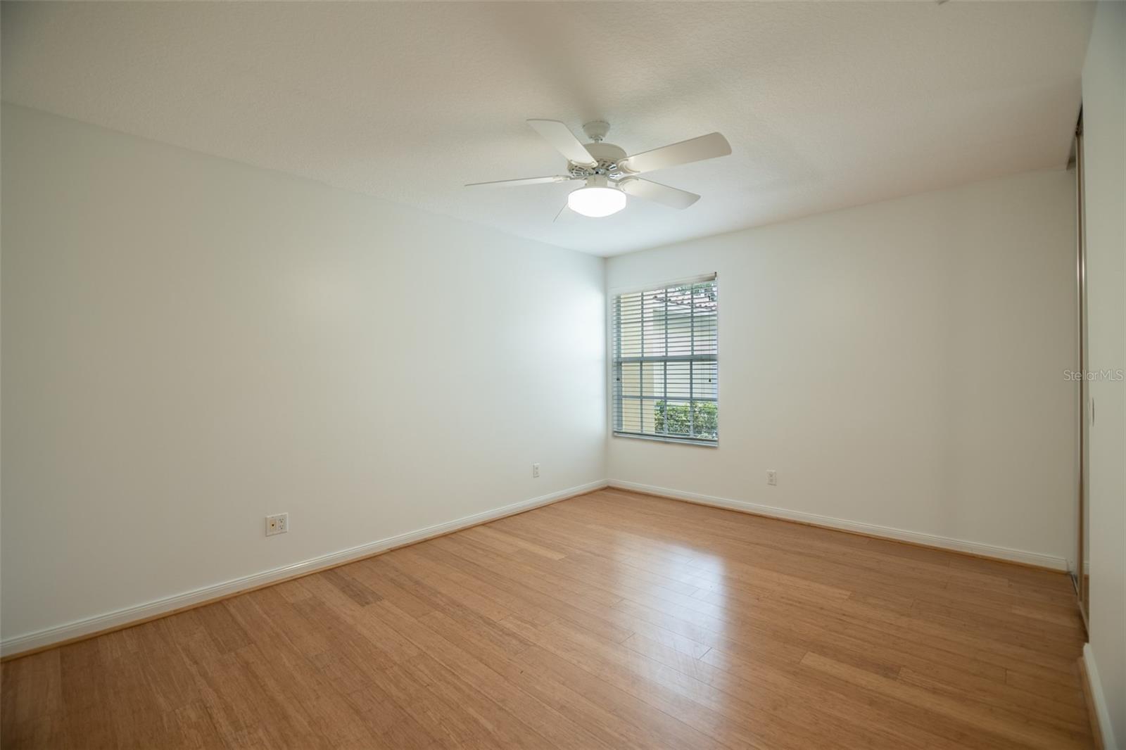Empty bedroom with wood-look flooring, a ceiling fan, and a window with blinds.
