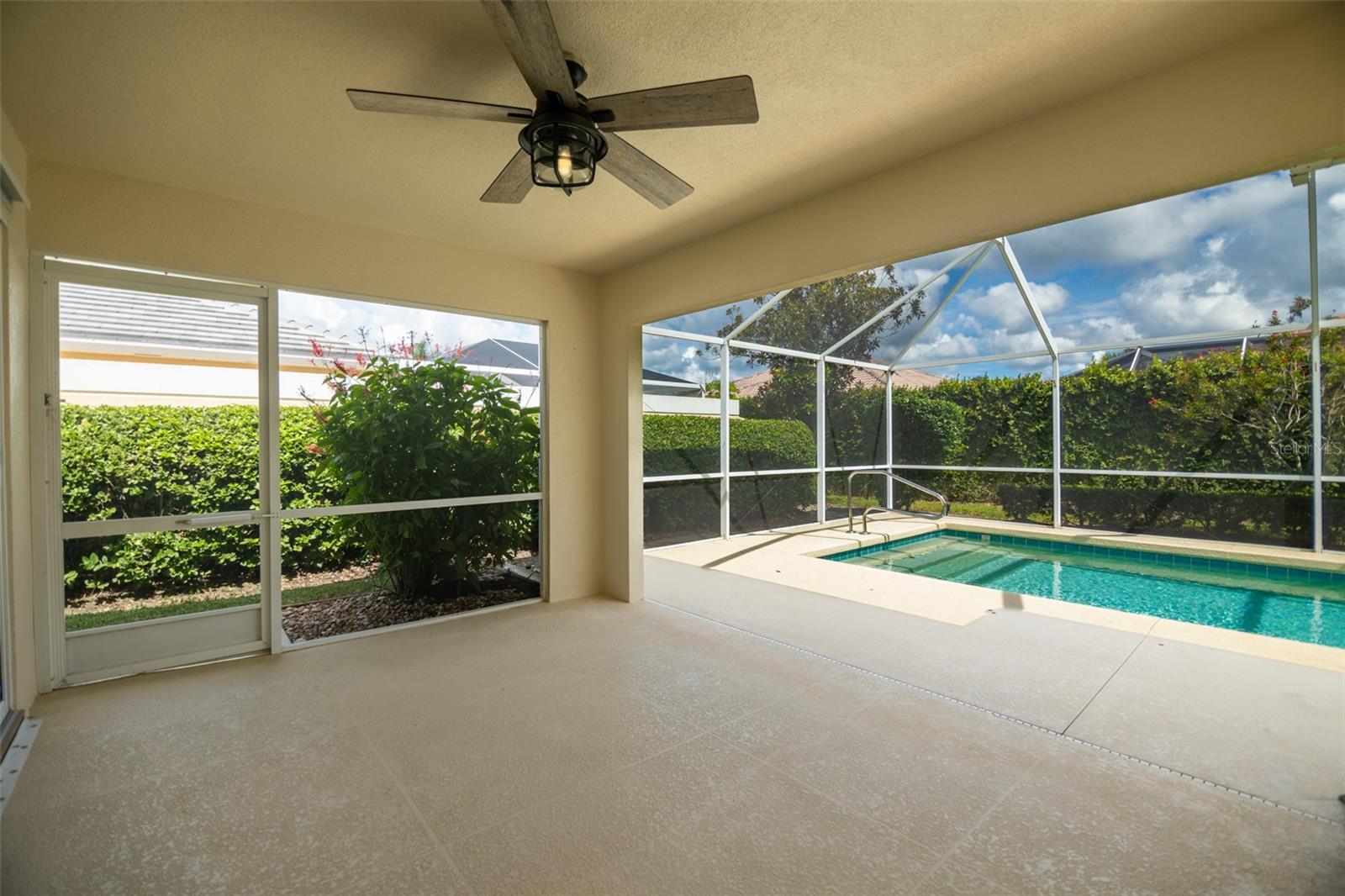 Screened lanai with a ceiling fan overlooking a private swimming pool and landscaped hedges.