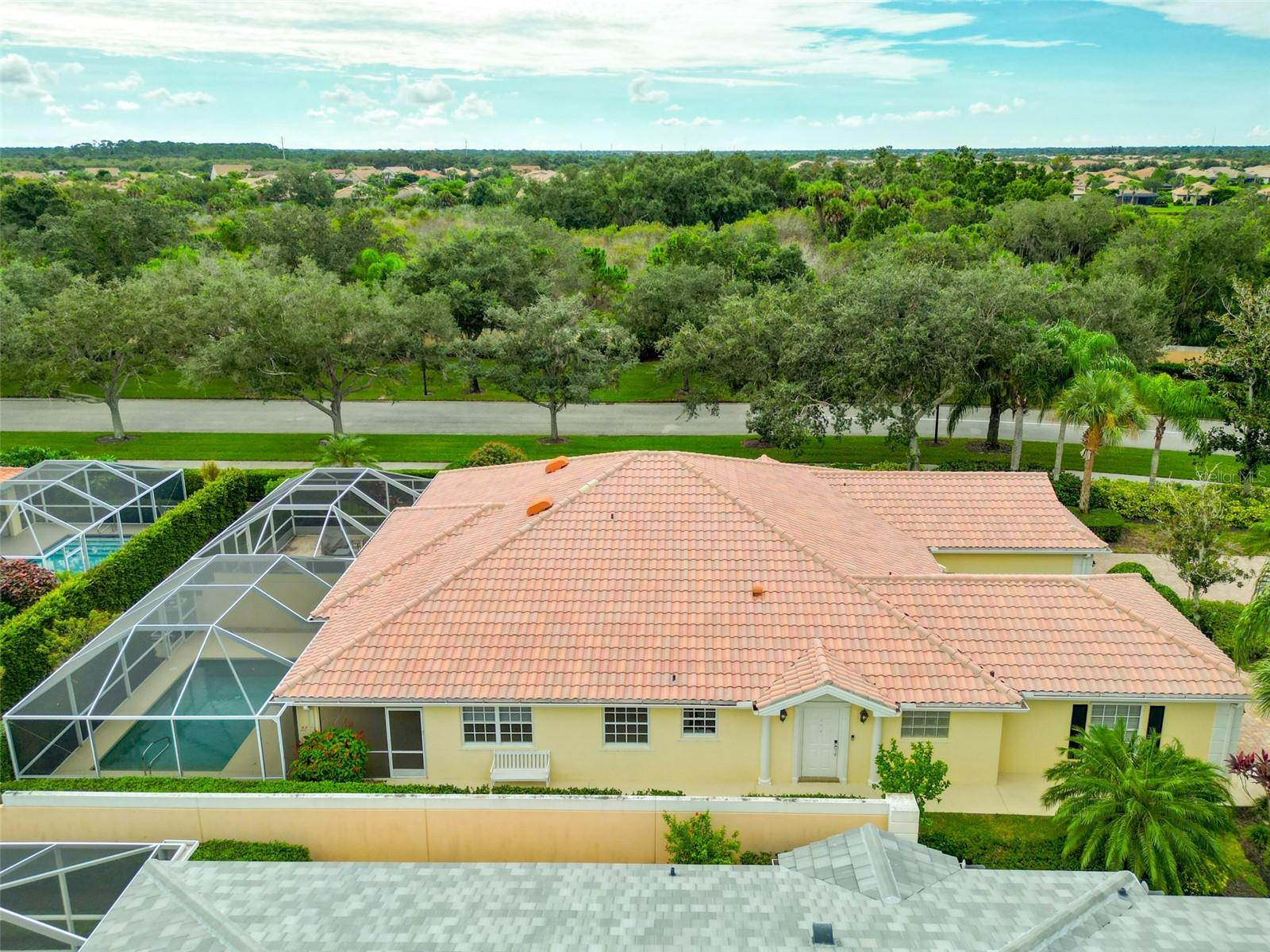 Aerial view of a tile-roofed home with a screened pool beside a wooded preserve.