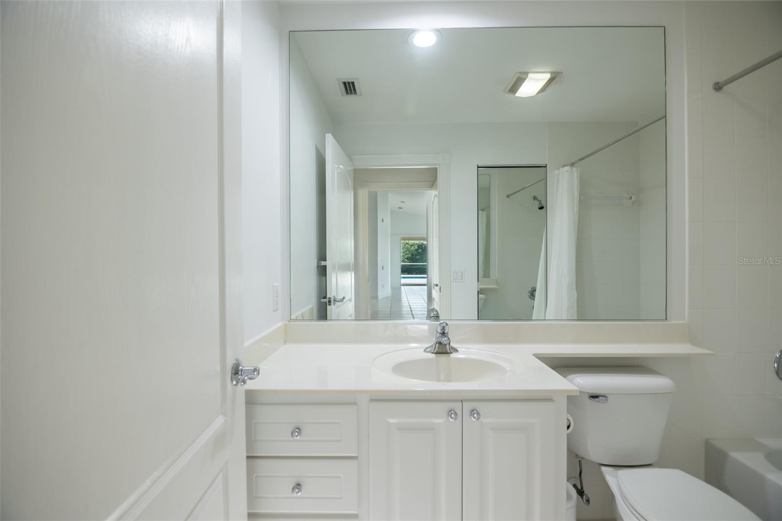White bathroom with a built-in vanity, large mirror, toilet, and tiled tub-shower area.