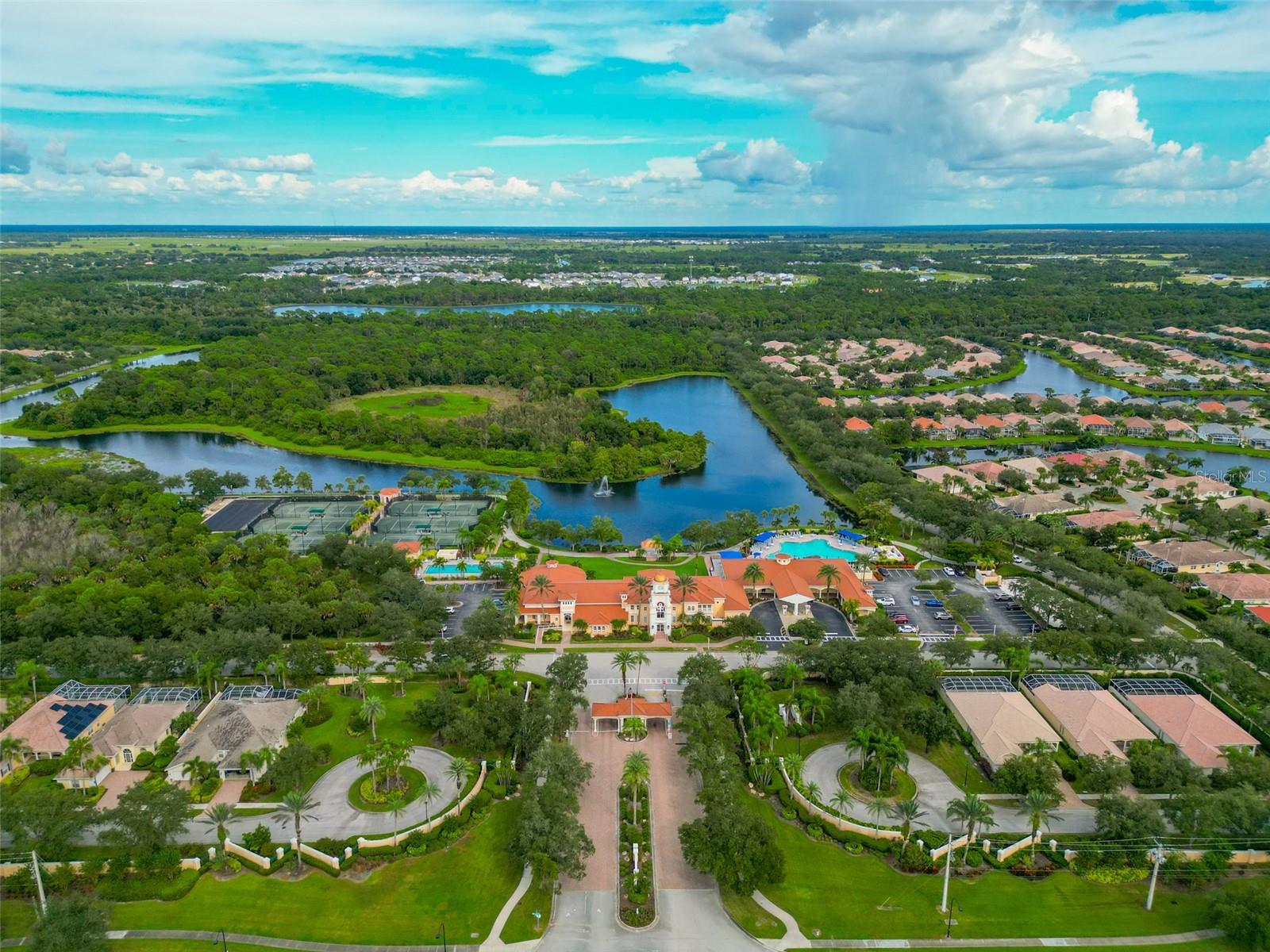 Aerial view of a Sarasota community with a clubhouse, pool, tennis courts, and lakes.