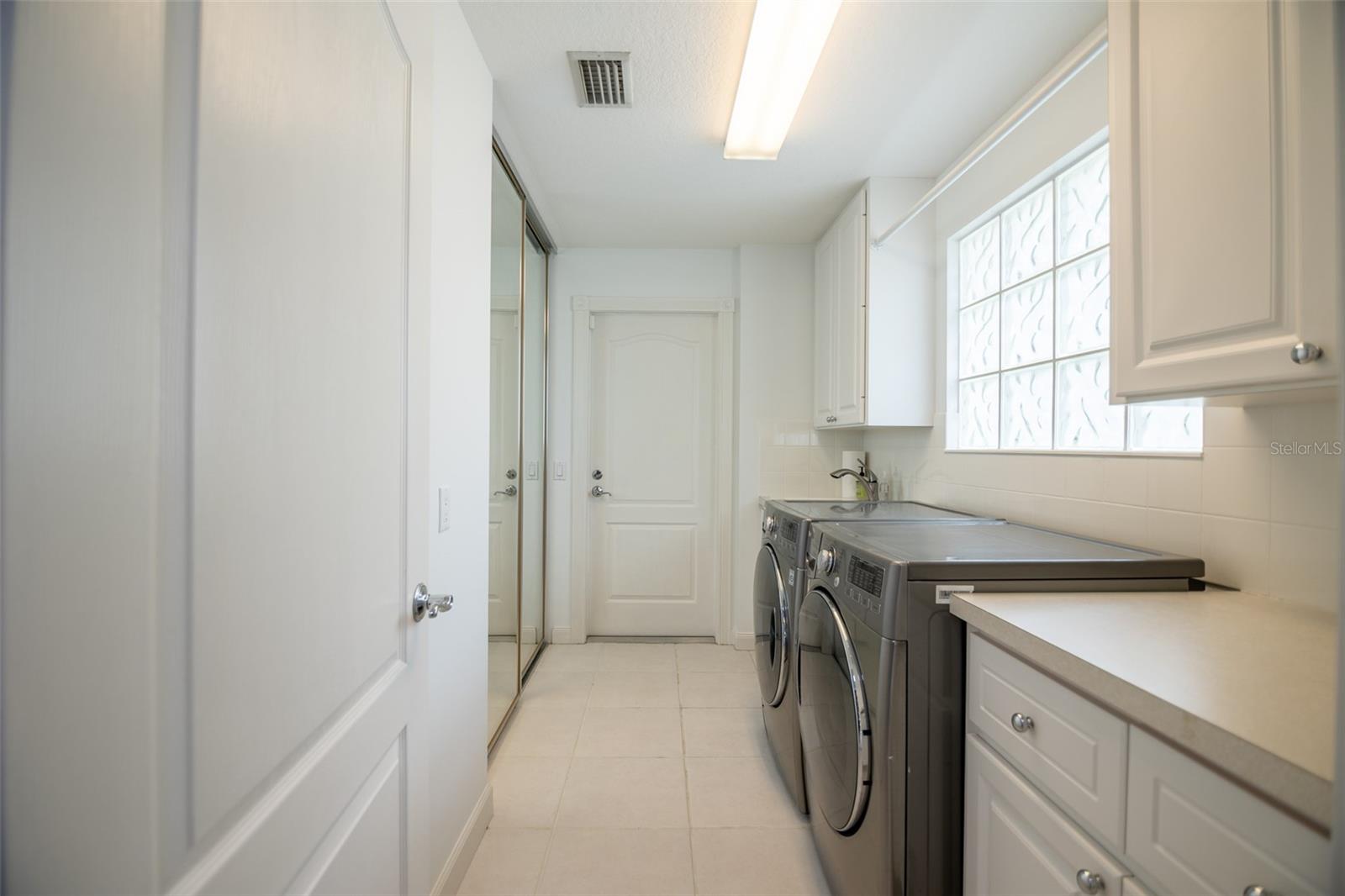 Laundry room with front-loading washer and dryer, white cabinetry, counter, and glass-block window.