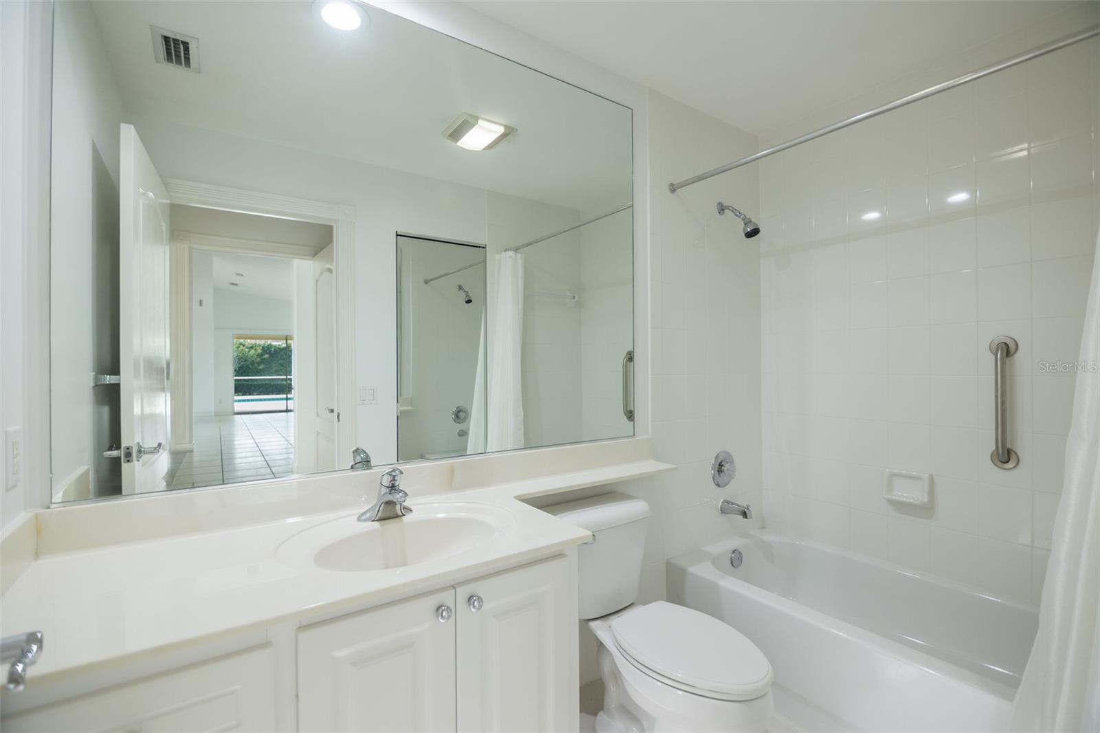 Bathroom with a white vanity, large mirror, and bathtub with tiled surround and grab bars.