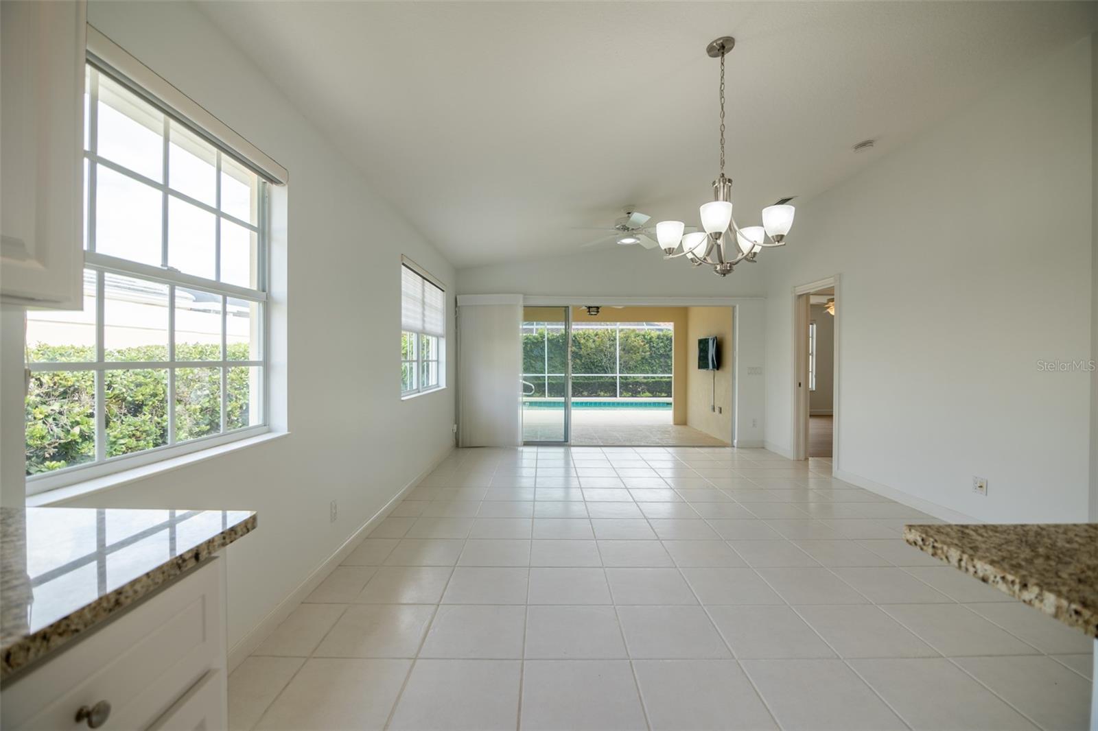 Vacant tiled dining area with chandelier, large windows, and sliding doors to a pool patio.
