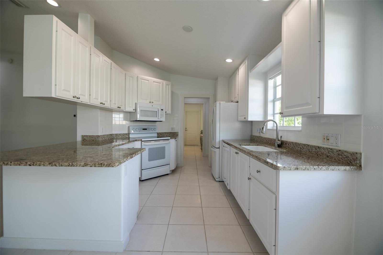 Kitchen with white cabinets and granite countertops, a central tiled walkway, and a window above the sink.