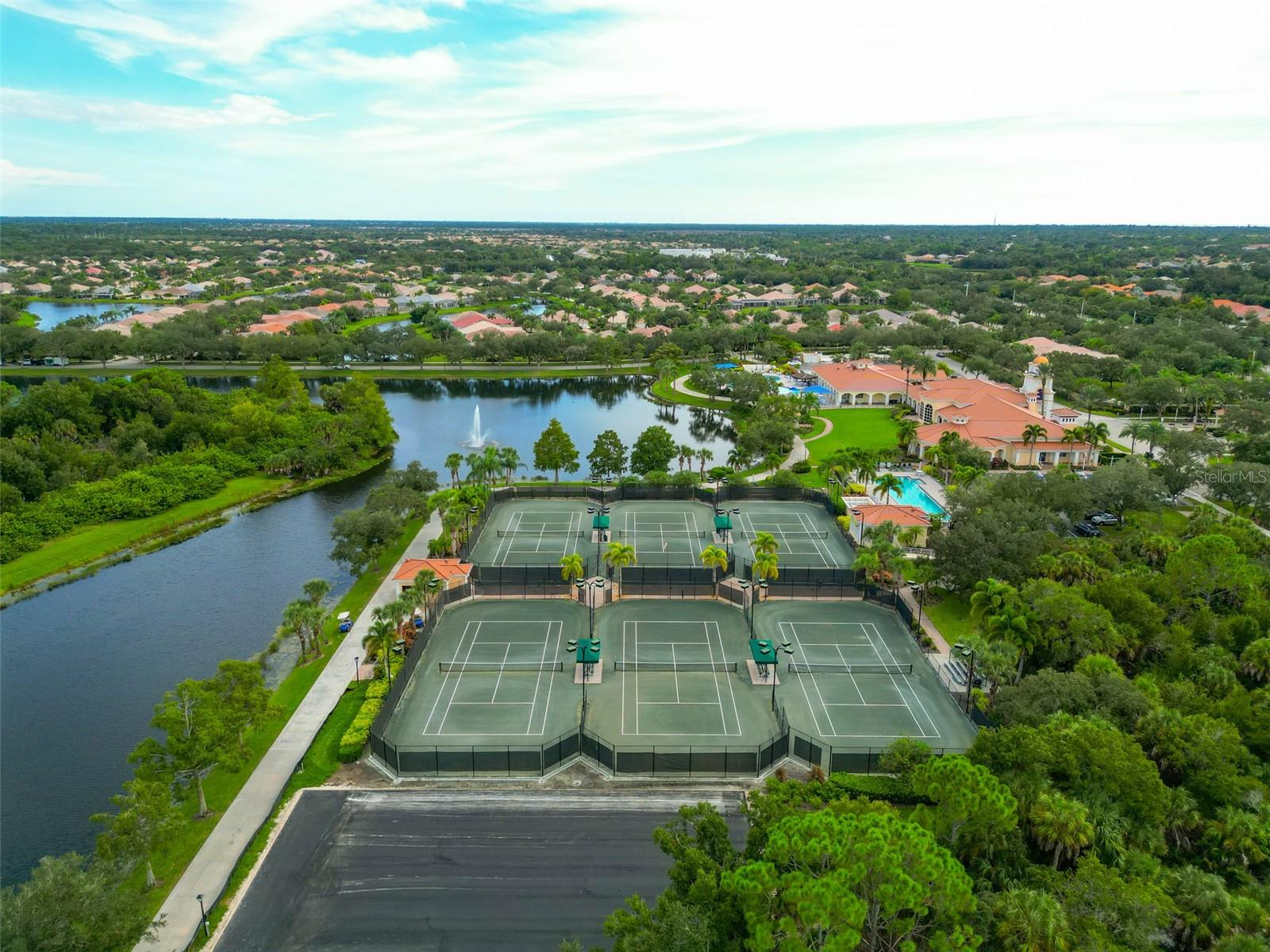 Aerial view of community tennis courts beside a lake, clubhouse, and swimming pool.