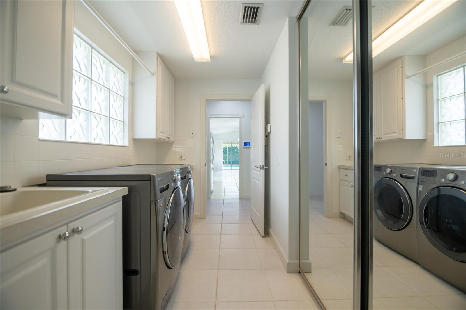 Laundry room with front-loading washer and dryer, utility sink, white cabinets, and mirrored sliding doors.