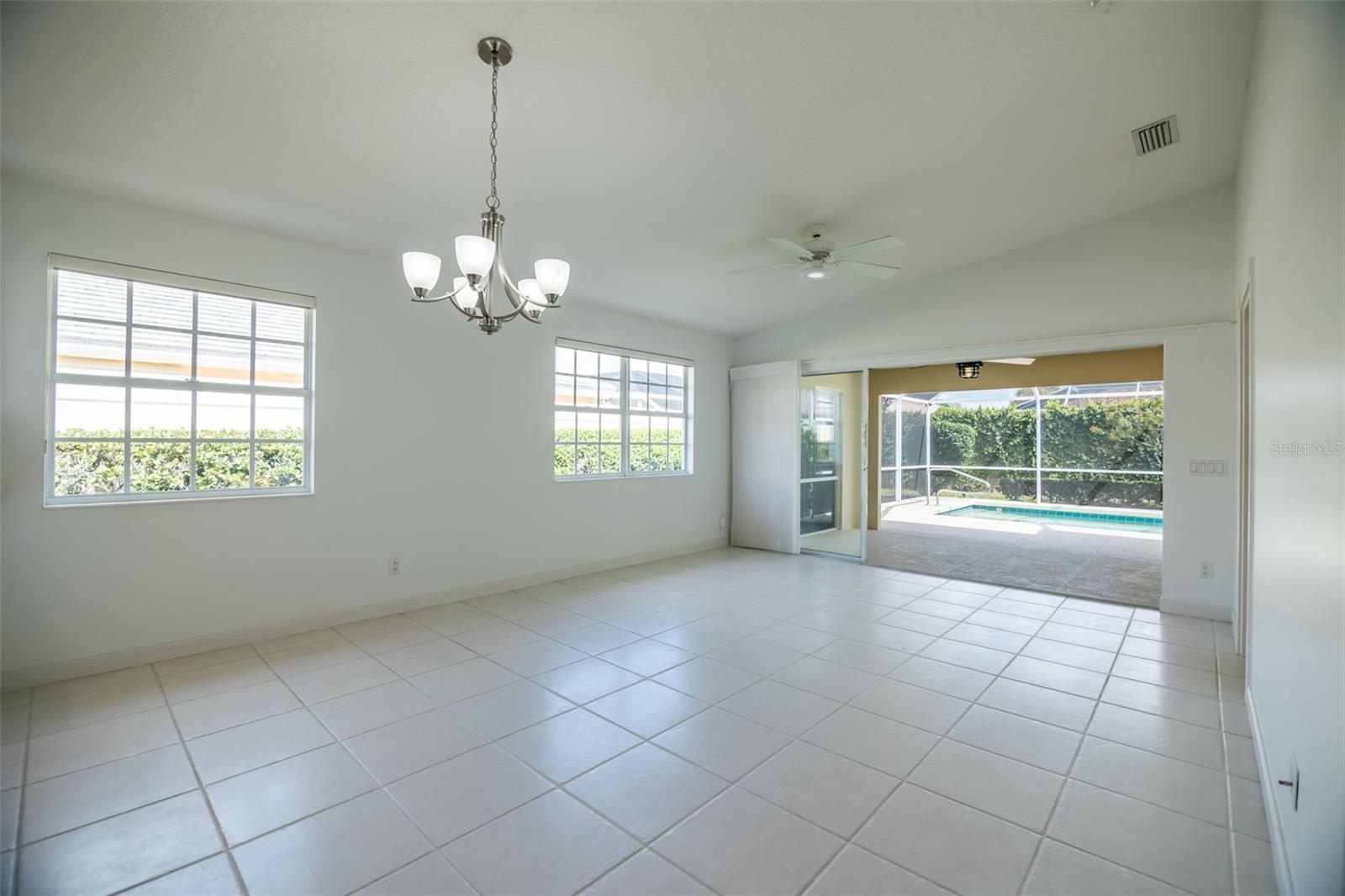Vacant tiled dining room with chandelier and sliding doors overlooking a screened patio and pool.