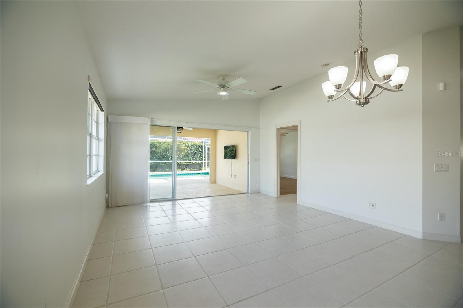 Empty tiled dining room with a chandelier and sliding doors overlooking a screened pool lanai.