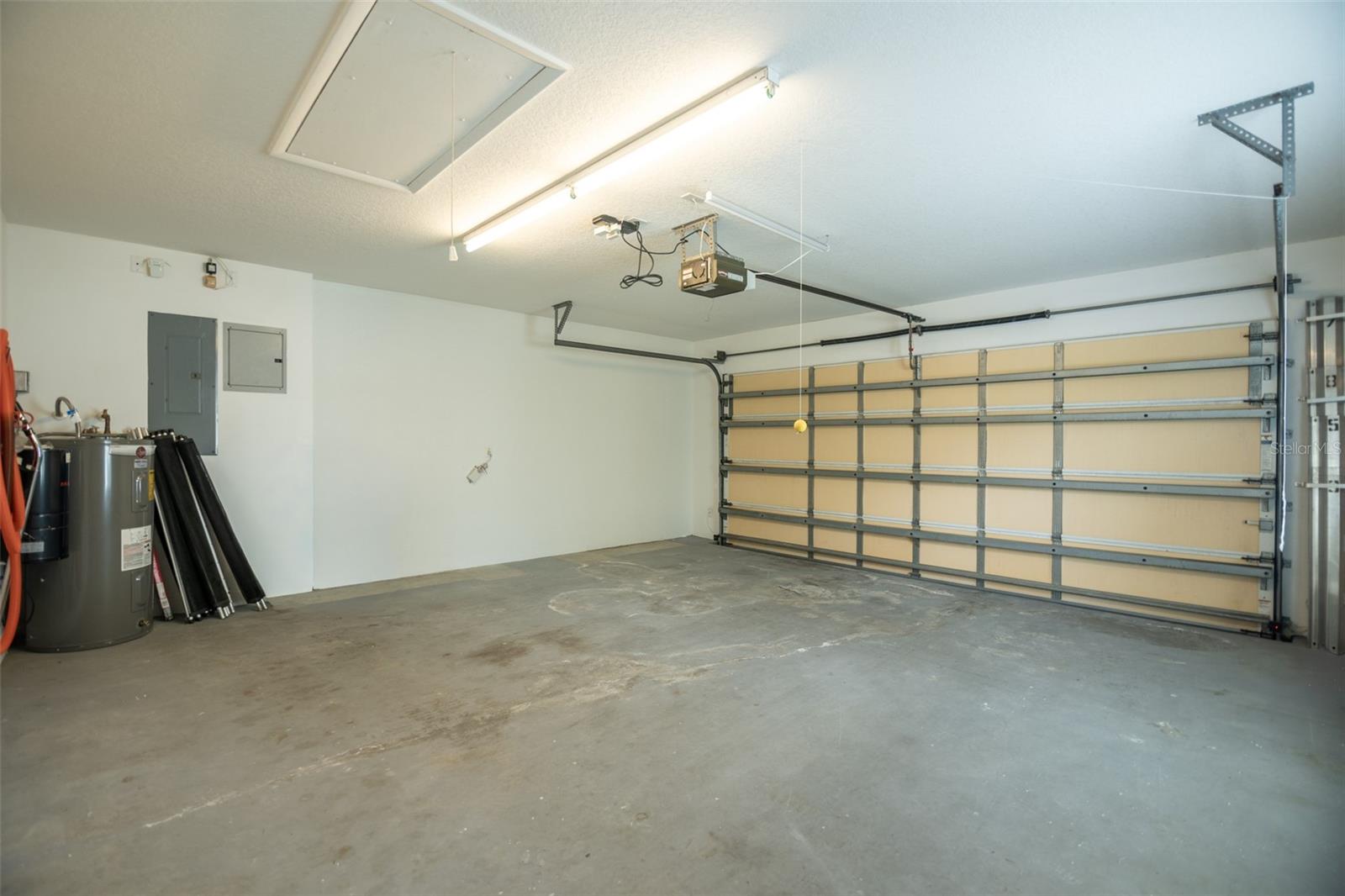 Empty garage with a large sectional door, concrete floor, and water heater.