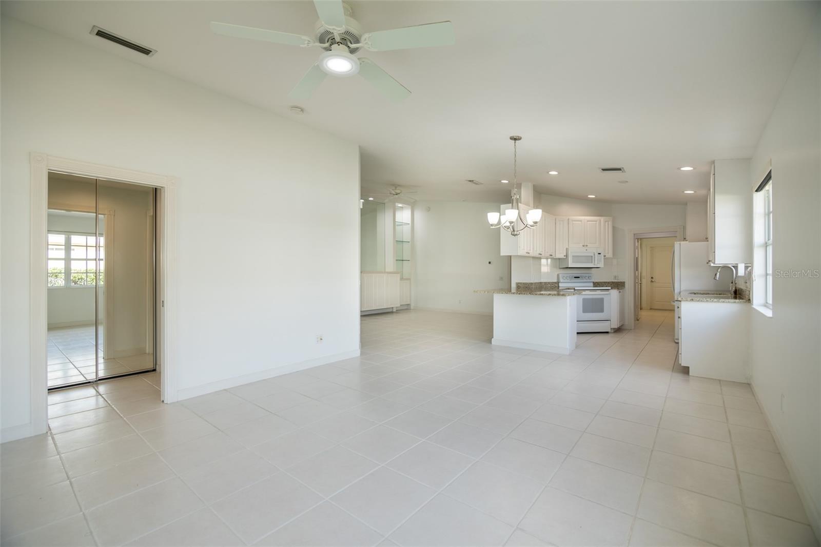 Open kitchen and dining area with white tile floors, granite counters, and a breakfast island.