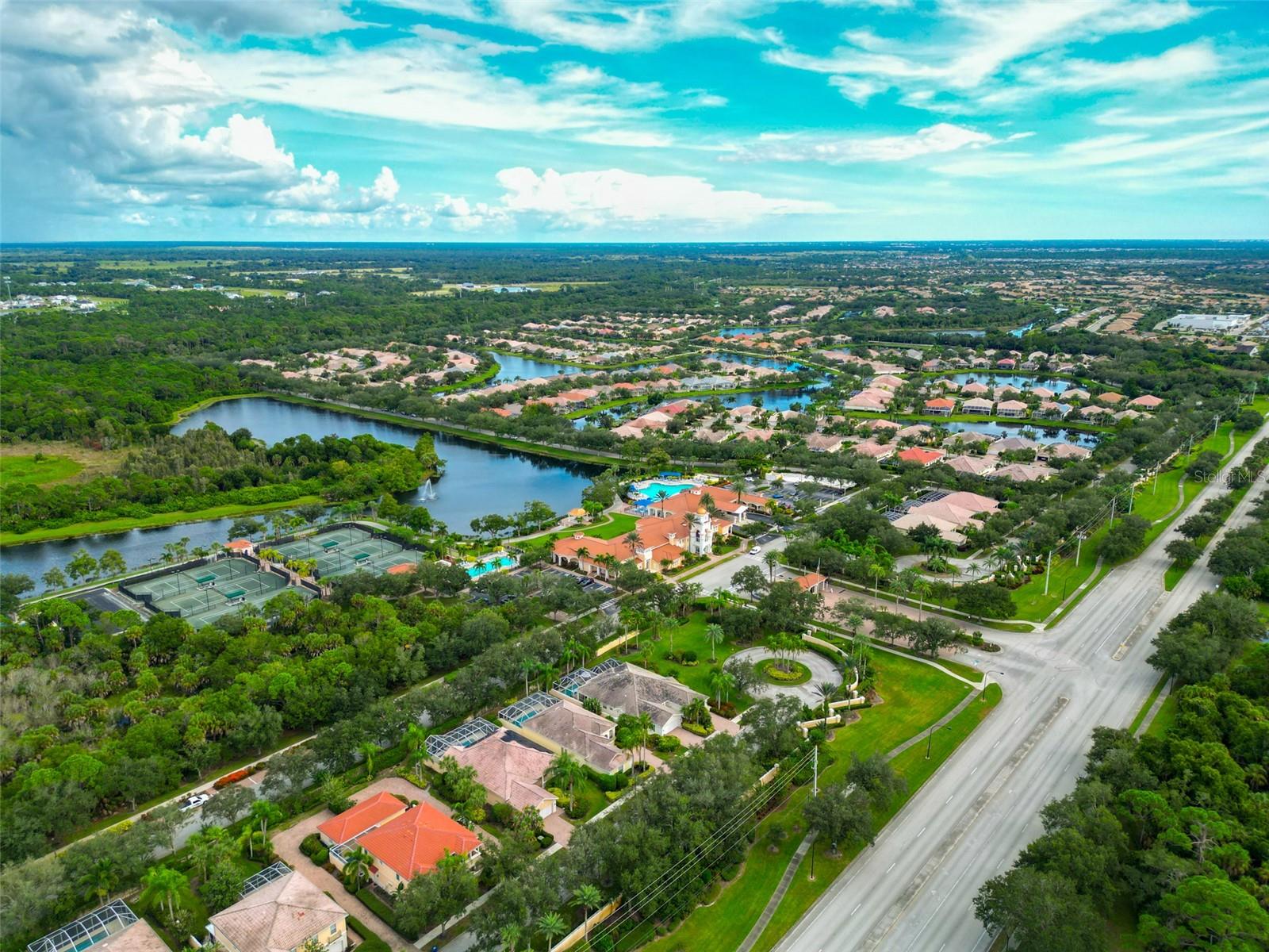 Aerial view of a Sarasota community with a lake, tennis courts, pool, and homes.