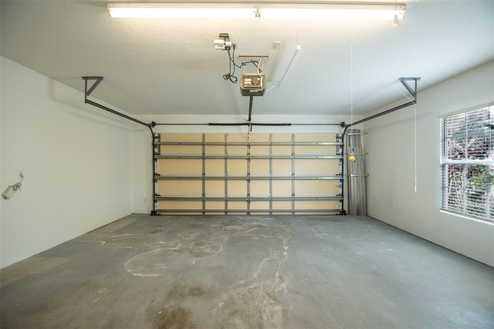 Empty garage with a closed sectional door, stained concrete floor, and window with blinds.