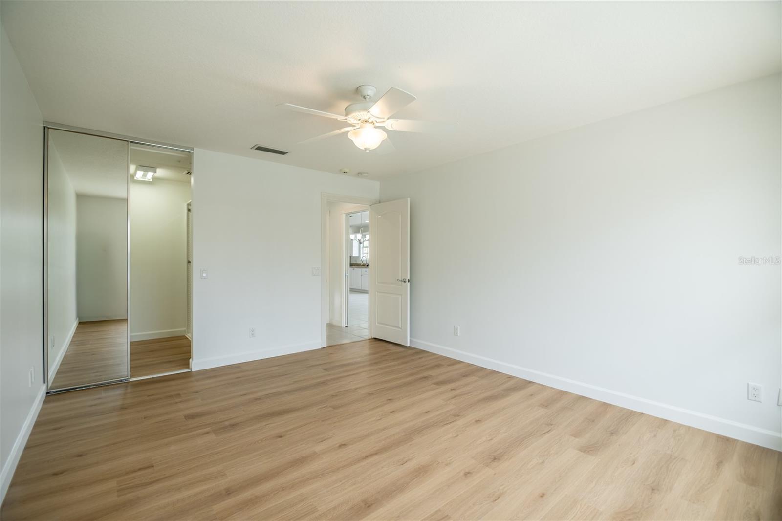Empty bedroom with wood-look floors, mirrored closet doors, and a ceiling fan with light.