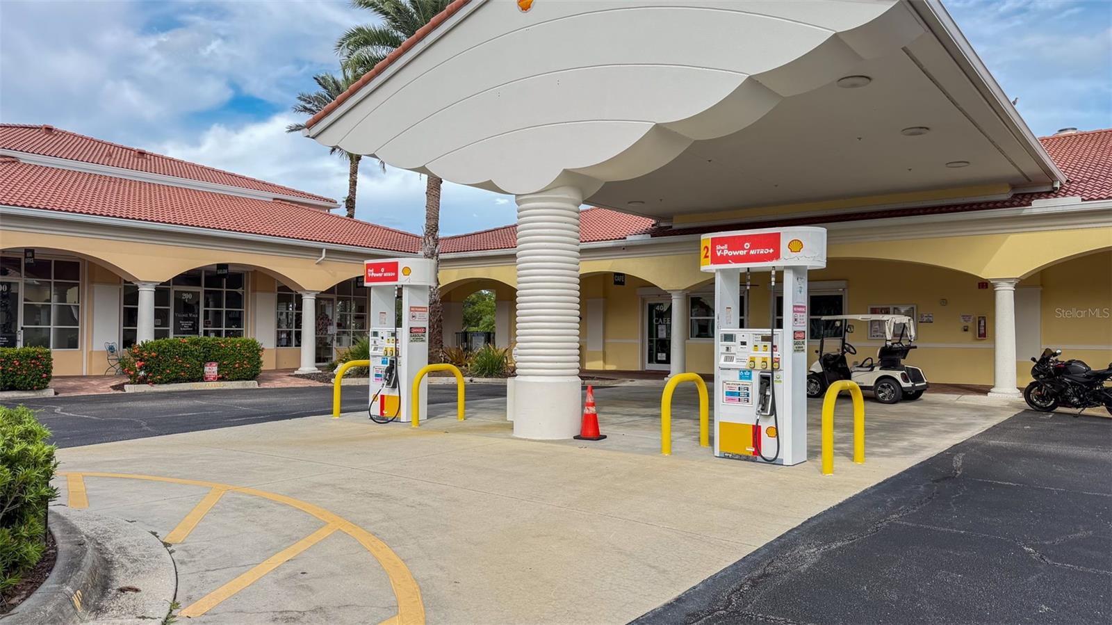 Covered Shell gas pumps in front of a yellow building with red tile roofs and parked golf carts.