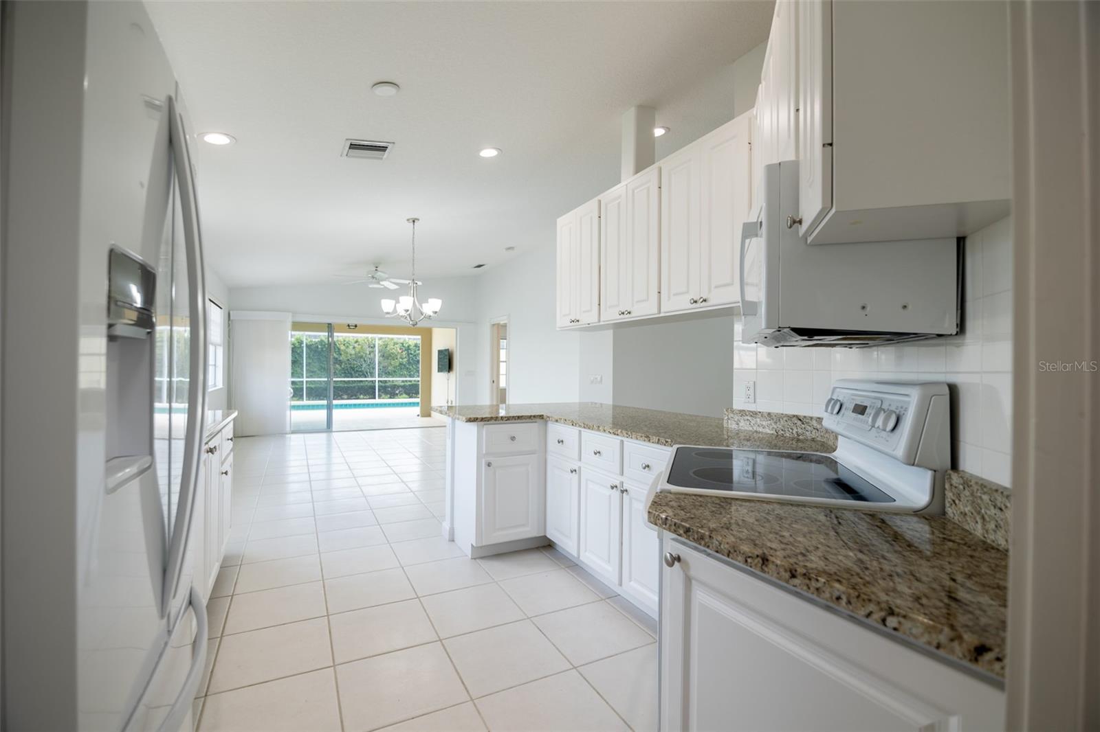 Kitchen with white cabinets and granite countertops opening toward a dining area and screened pool.