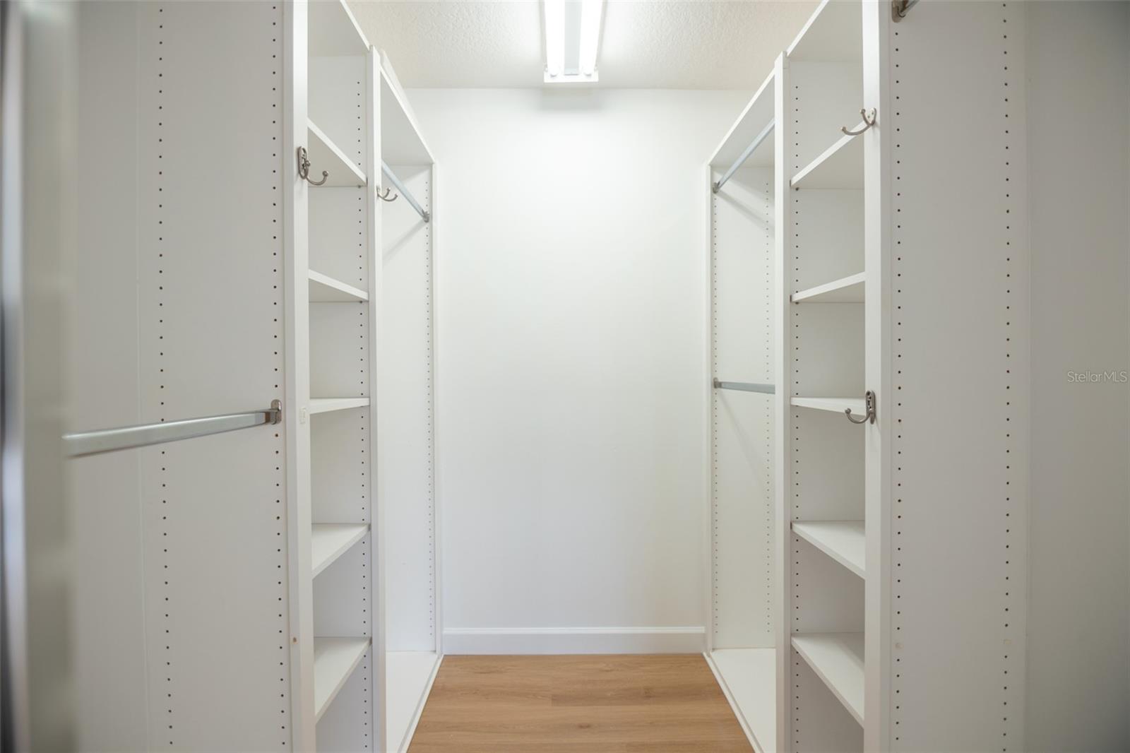 Walk-in closet with white adjustable shelving and hanging rods on both sides, plus wood-look flooring.