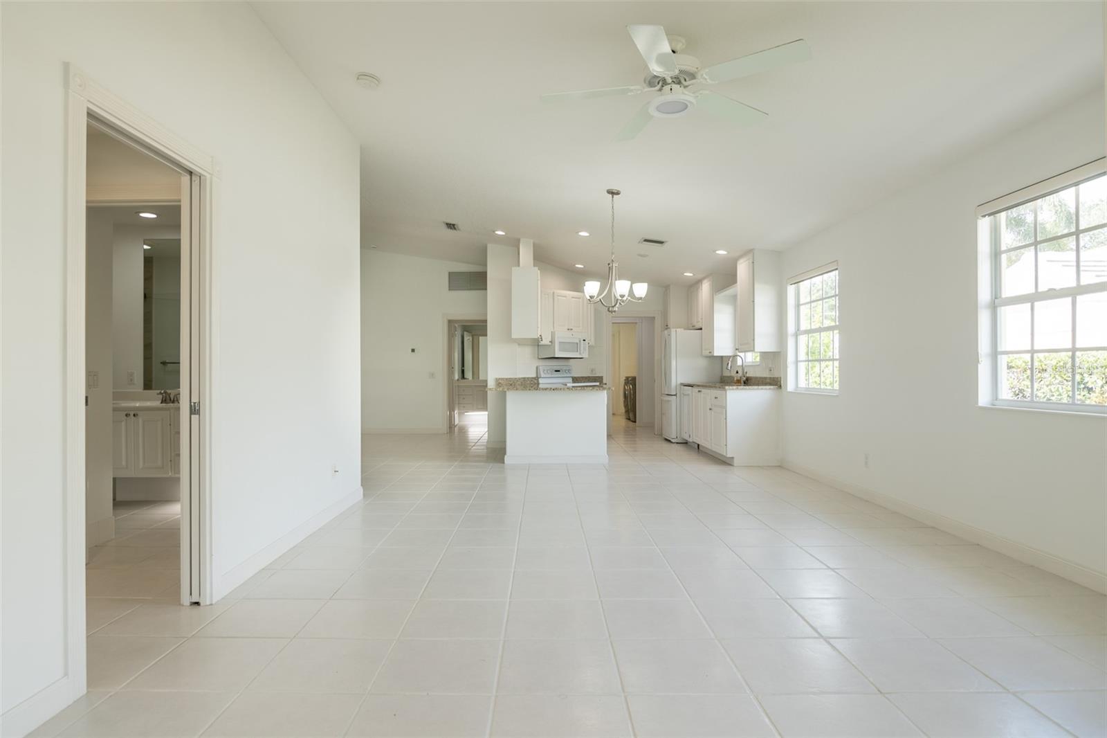 Vacant kitchen and dining area with a central island, white cabinetry, tile floors, and large windows.