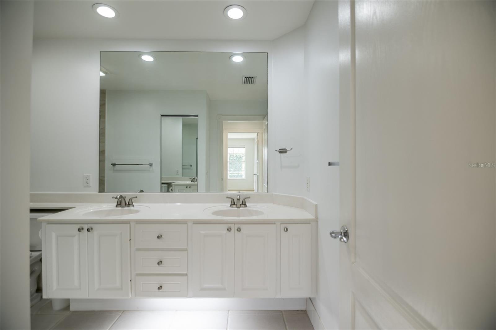 Bathroom with a white double-sink vanity, paneled cabinets, and a large mirror.