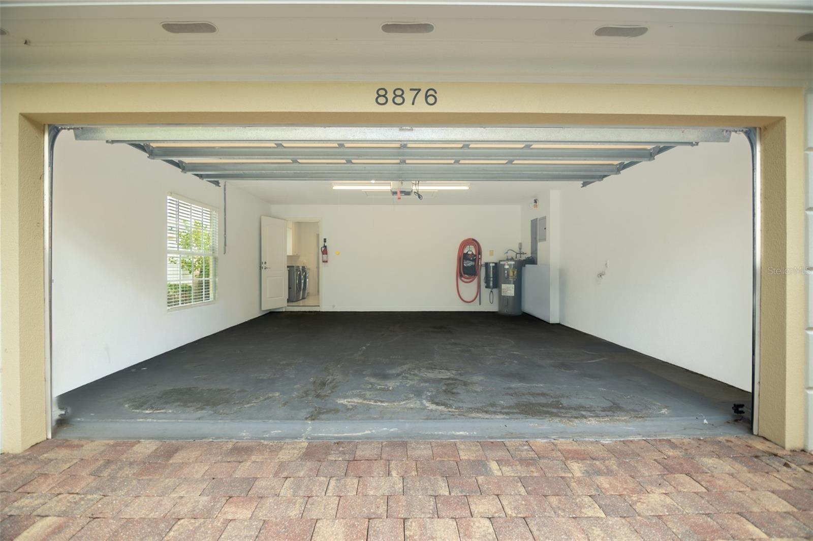 Open two-car garage with a concrete floor, raised door, side window, and laundry area beyond.