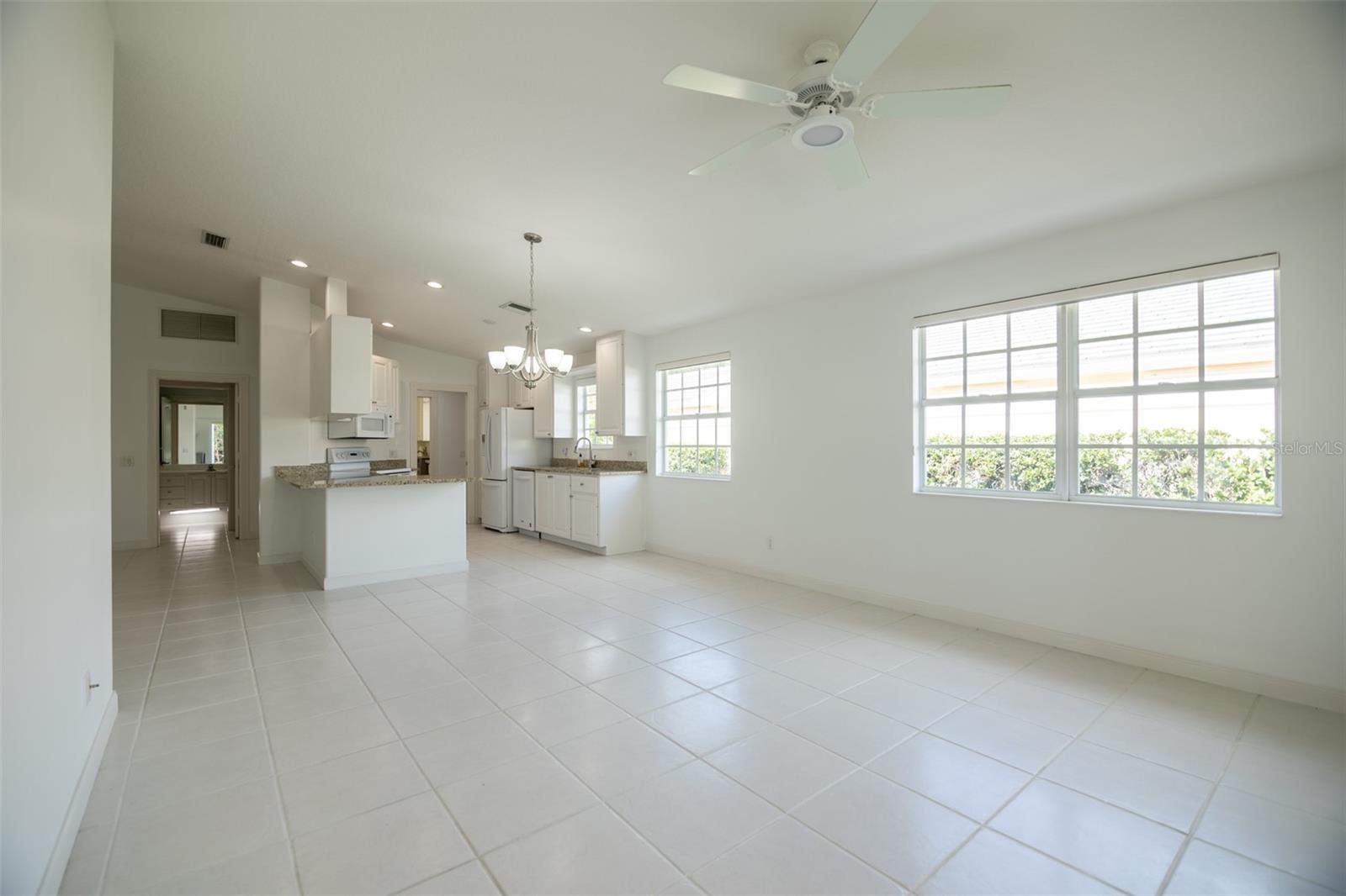 Vacant kitchen and dining area with white tile floors, granite counters, and large windows.