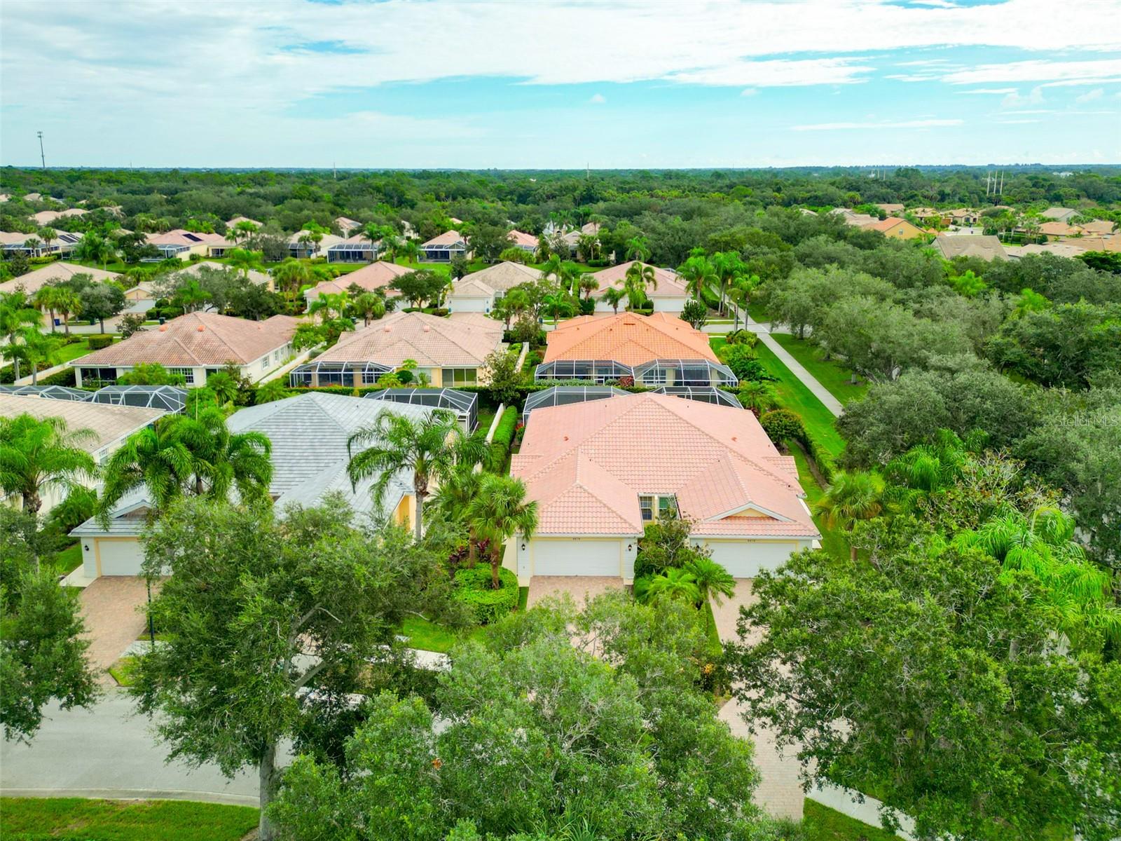 Aerial view of tile-roof homes and screened lanais in a leafy Sarasota neighborhood.