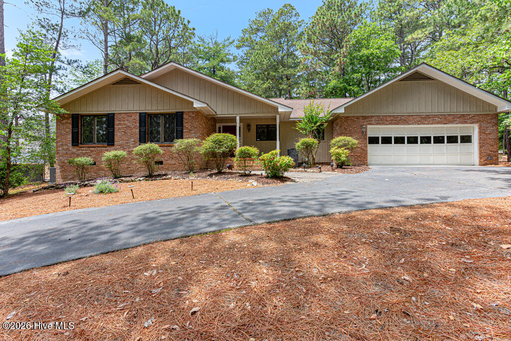 Single-story brick home with a white double garage door and mature trees.