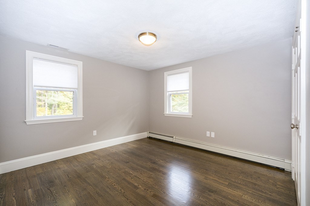 Vacant room with dark hardwood floors, gray walls, and two windows.