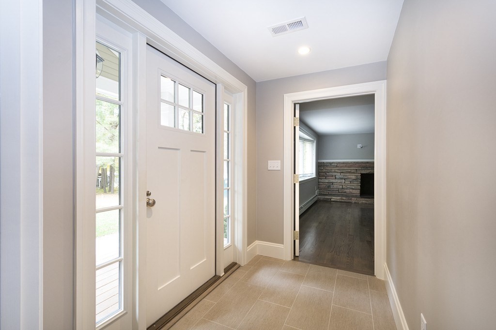 Empty tiled entryway with a white front door and glass sidelights, opening to a room with a stone fireplace.