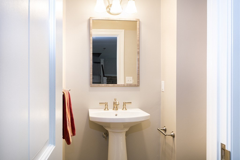 Bathroom with a pedestal sink, brass faucets, framed mirror, and red towel.