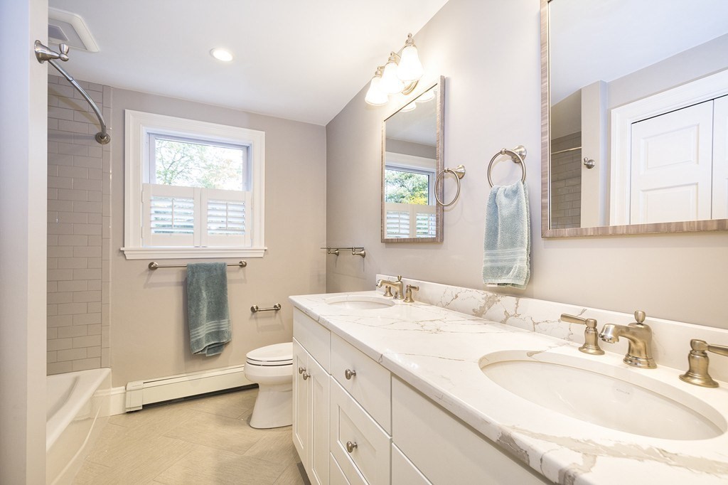 Bathroom with a marble double vanity, large mirrors, and a tiled tub and shower.