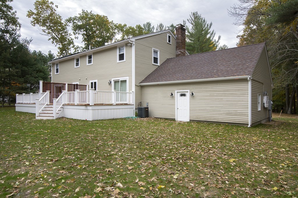 Rear of a beige two-story house with a raised white deck and a leaf-strewn lawn.