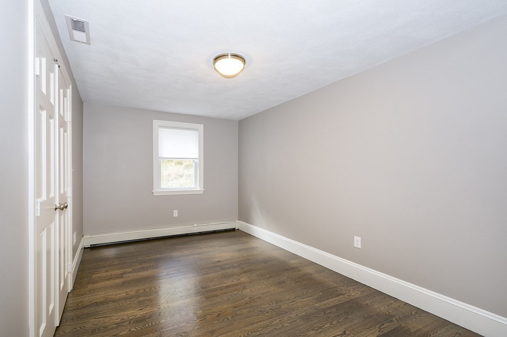 Empty bedroom with dark hardwood floors, a window, and white closet doors.