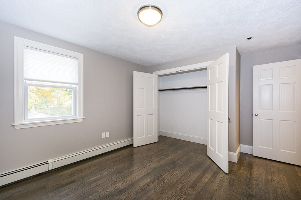 Vacant bedroom with dark hardwood floors, a window, and an open double-door closet.