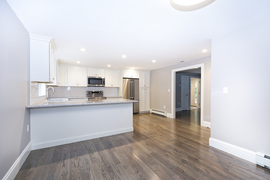 Kitchen with white cabinets, stainless steel appliances, and a stone-topped peninsula beside hardwood flooring.