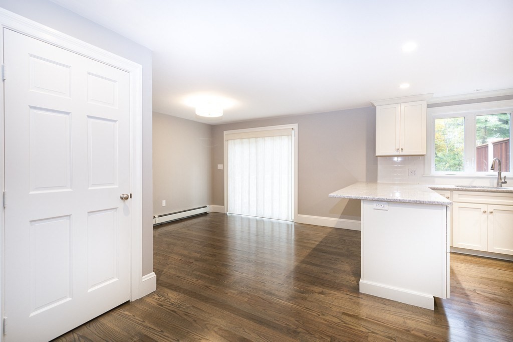 Vacant kitchen and dining area with white cabinets, a stone-counter peninsula, and dark wood floors.