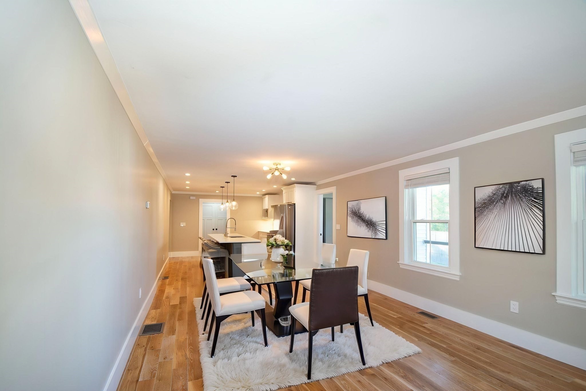 Dining area with a glass table and white rug opening onto a modern kitchen.