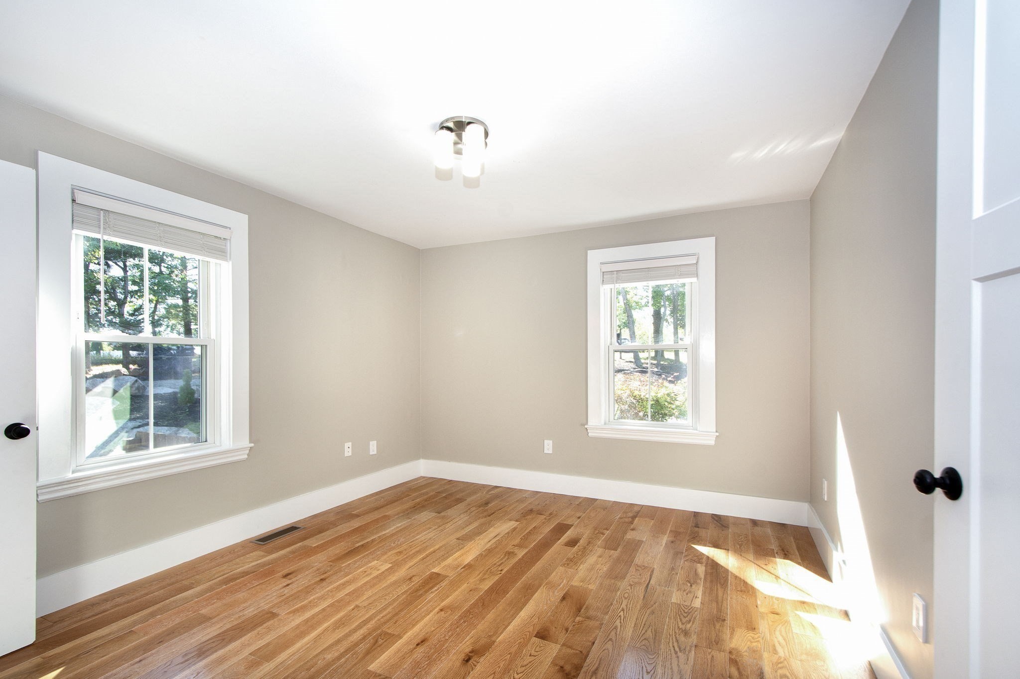 Empty room with hardwood floors, beige walls, and two windows.