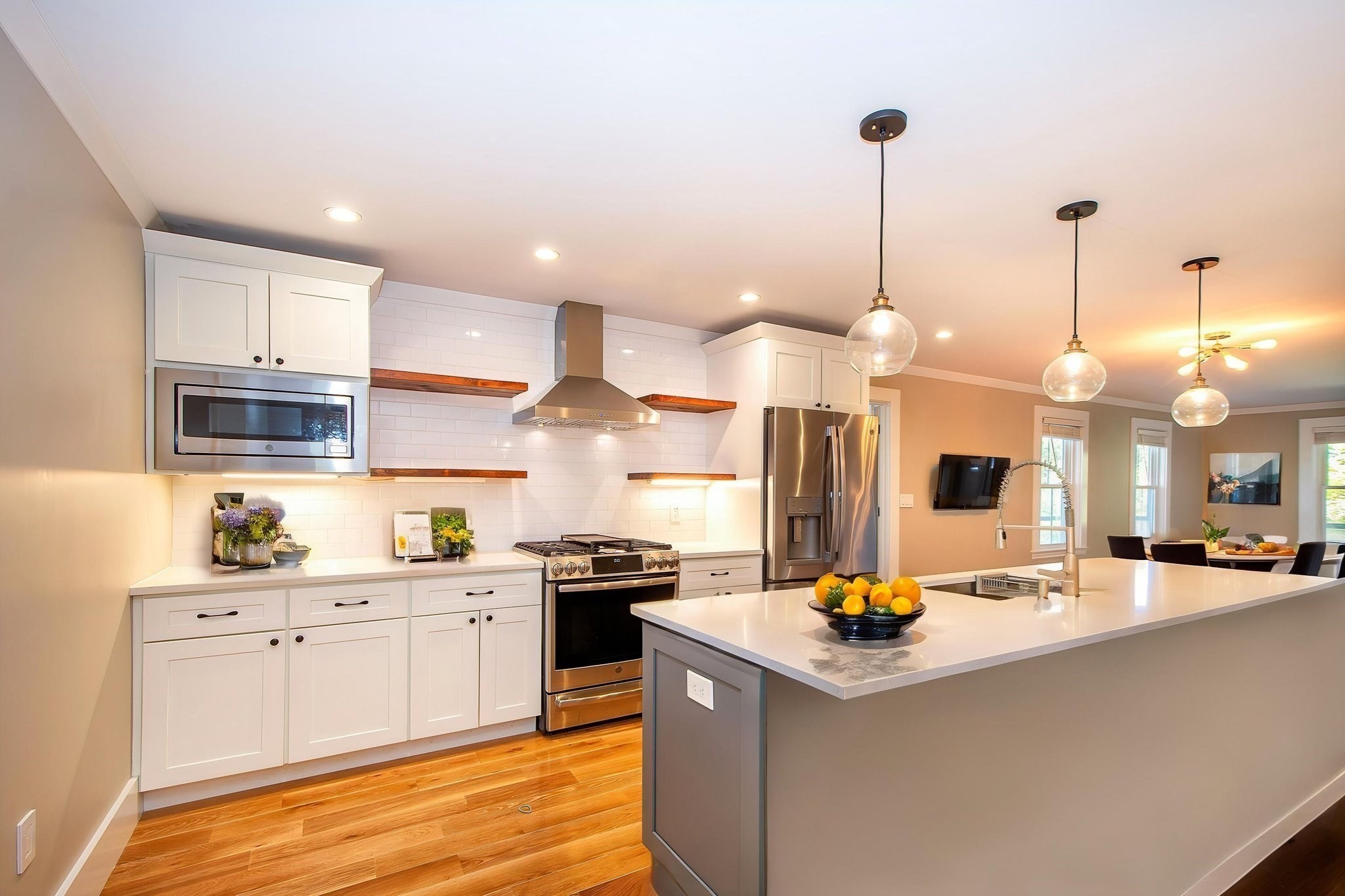 Open-plan kitchen with white cabinets, a large island, stainless steel appliances, and wood floors.