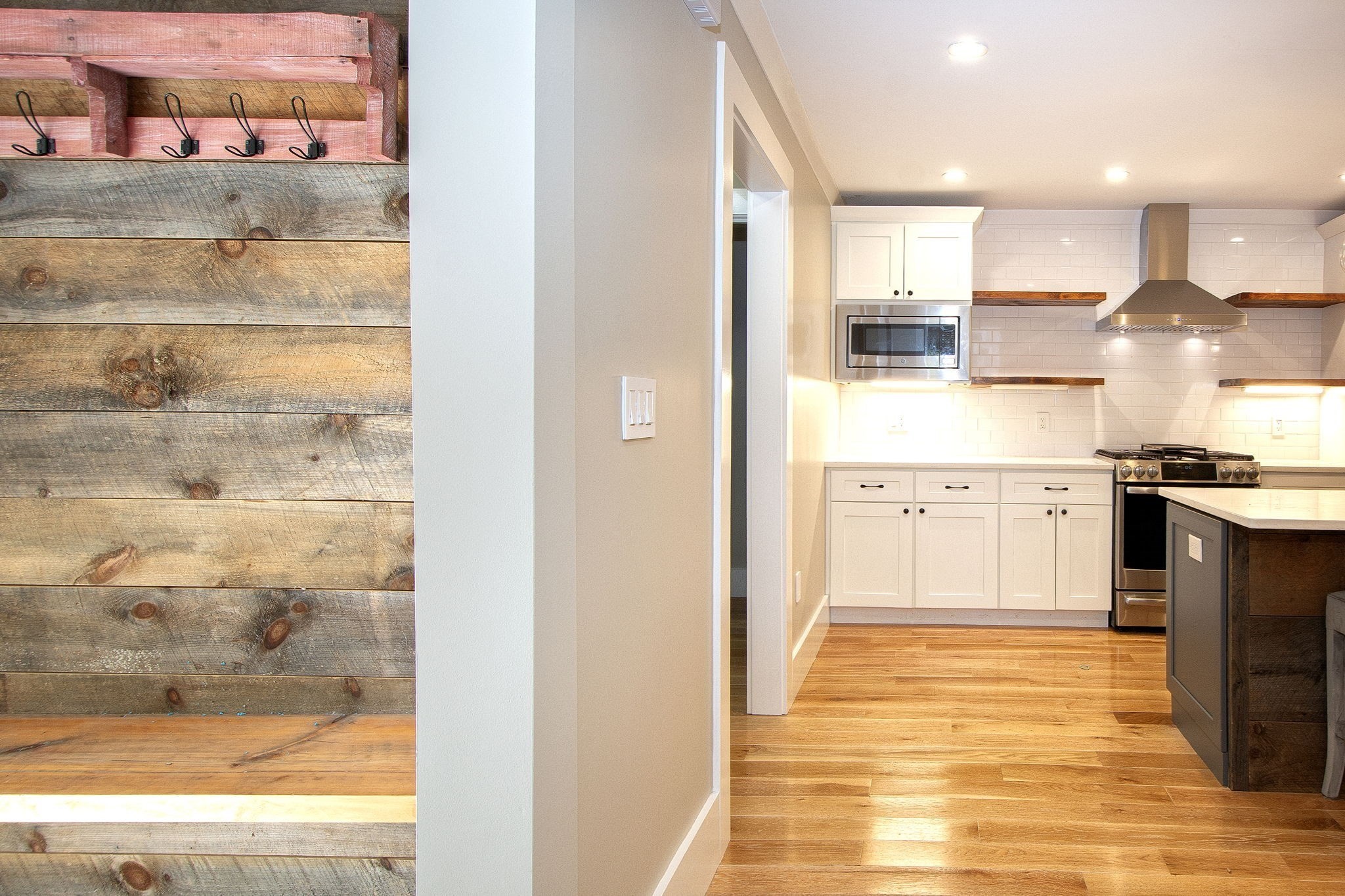 Kitchen with white cabinets, stainless appliances, hardwood floors, and a rustic reclaimed-wood wall with hooks.