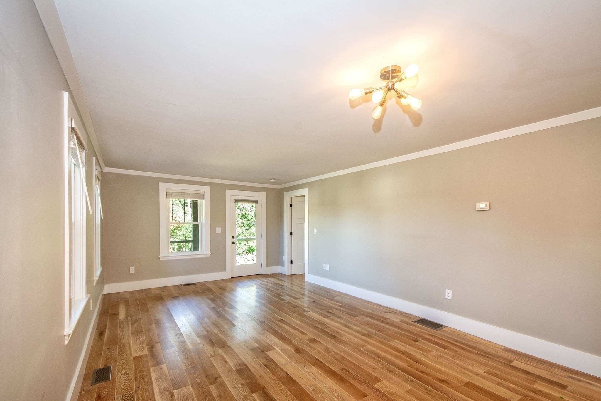 Vacant living room with hardwood floors, tall windows, and a glass-paneled exterior door.