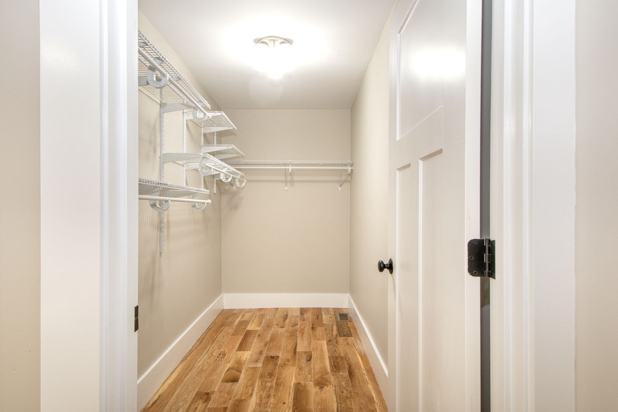 Walk-in closet with built-in wire shelving and warm-toned hardwood floors.