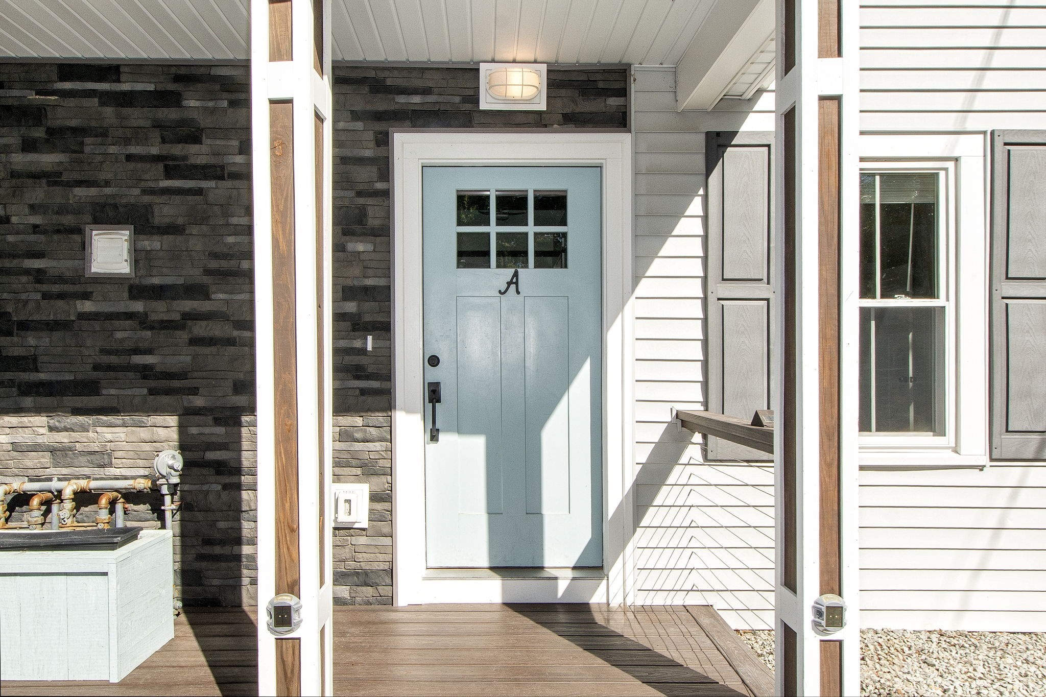 Covered home entry with a pale blue door marked A, dark stone veneer, and a wood deck.