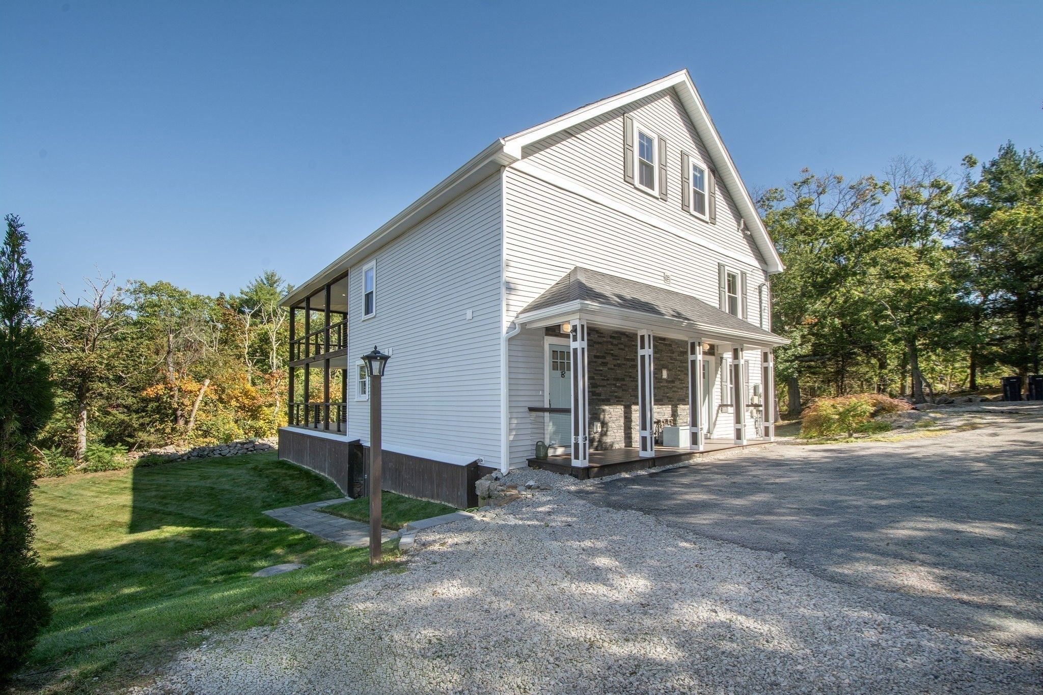 White two-story home with a covered porch, screened side porch, and gravel driveway.